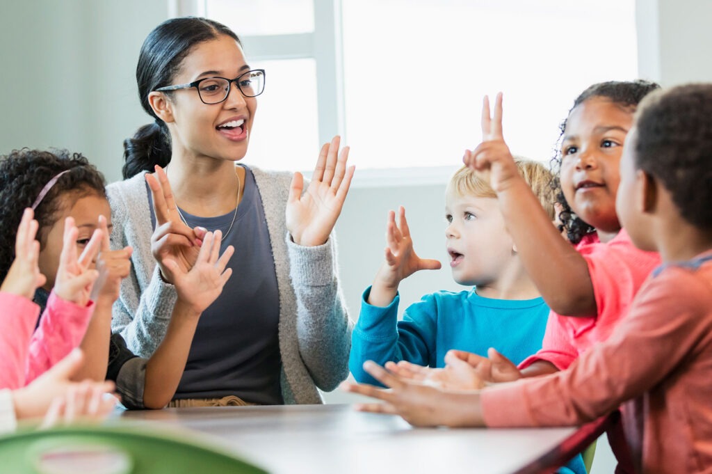 Group of kindergarten kids clapping with a teacher.